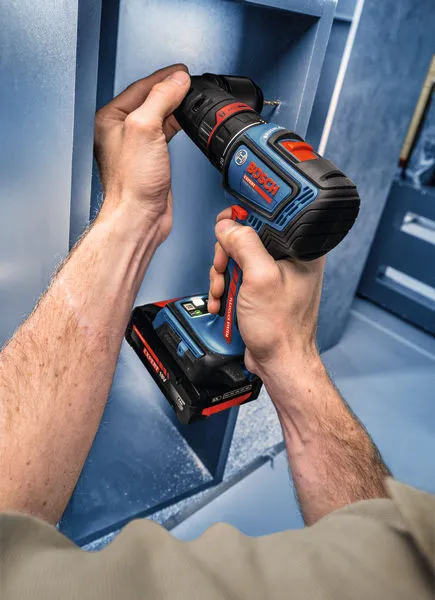 En person bruger en batteridrevet boremaskine til at samle en blå metalreol.